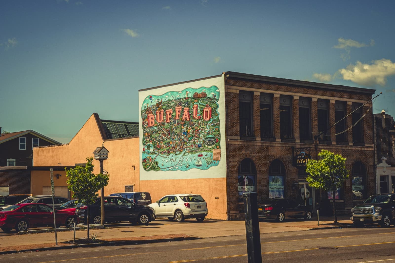 A sunny Buffalo street with a colorful 'BUFFALO' wordmark mural on a brick building.